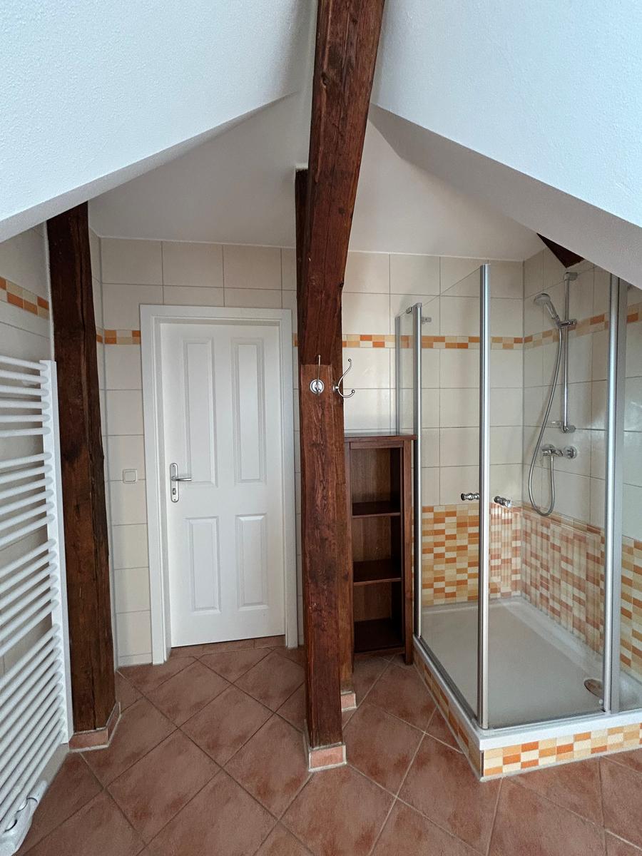Dusche mit Glaswand, Holzbalken und Fliesenboden im Dachgeschossbad.