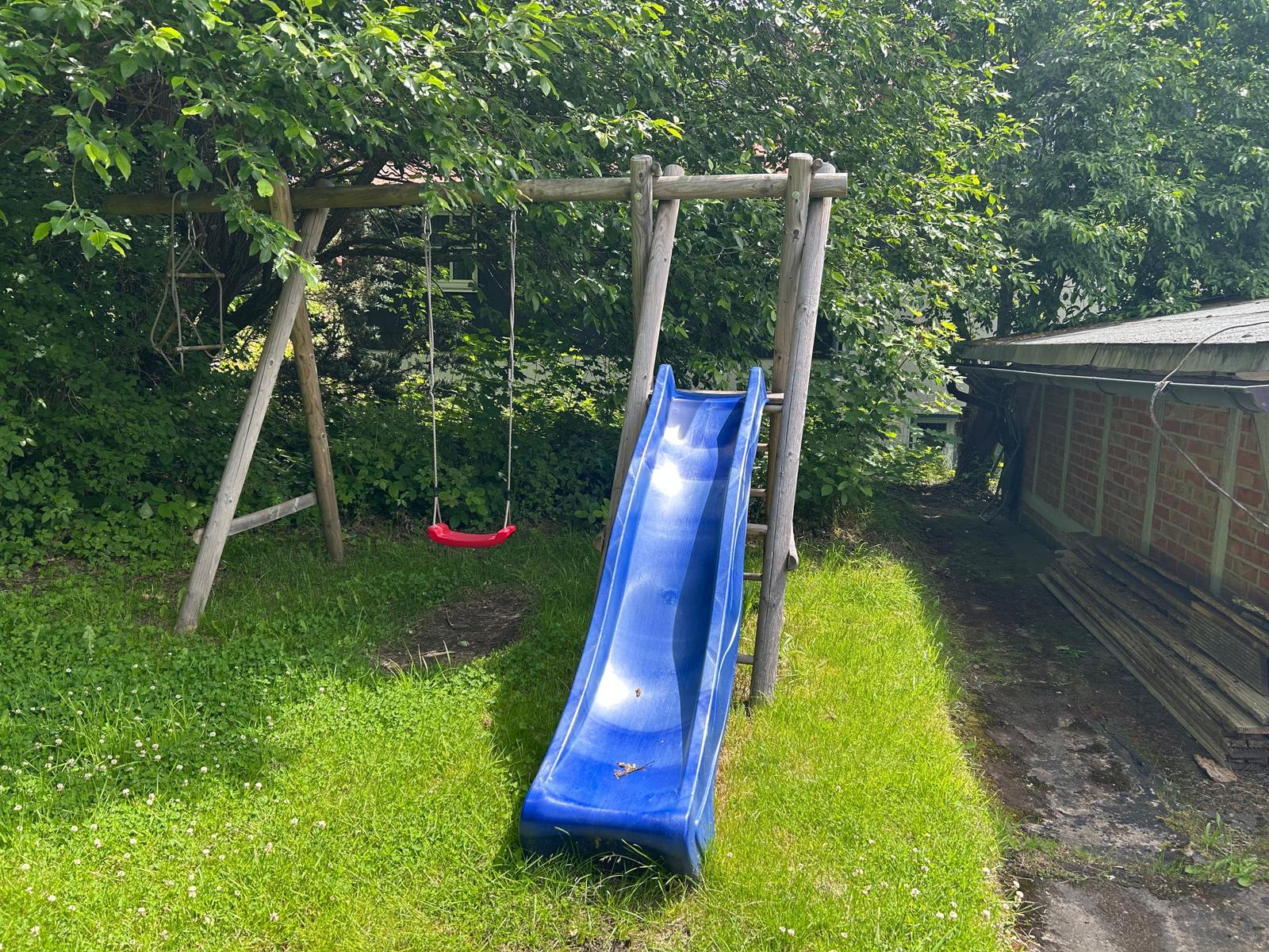 Blauer Rutschbahn und Schaukel im Garten mit grünem Rasen und Bäumen.