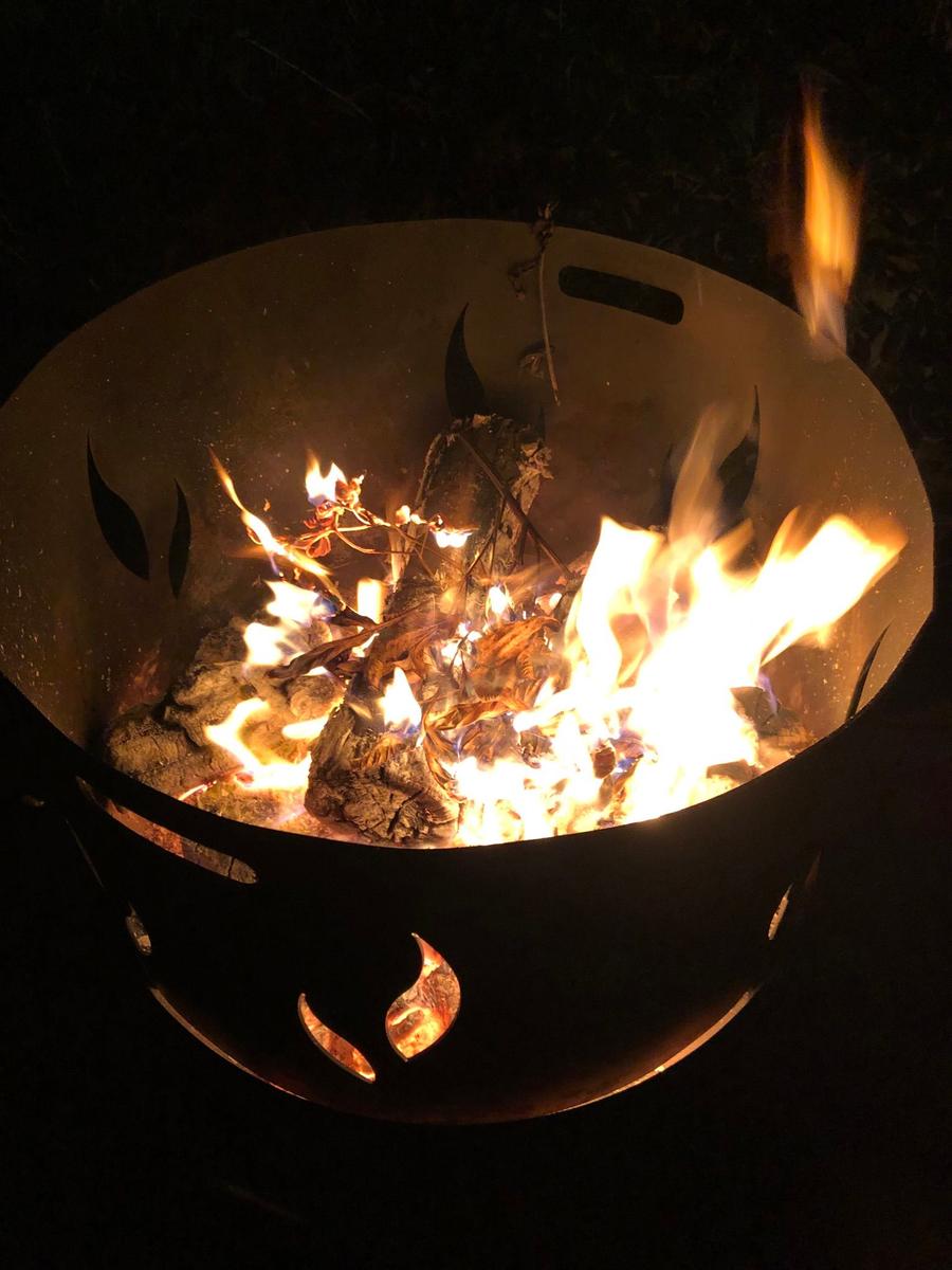 Ein brennender Feuerkessel mit Holz und Flammen im Freien bei Nacht.