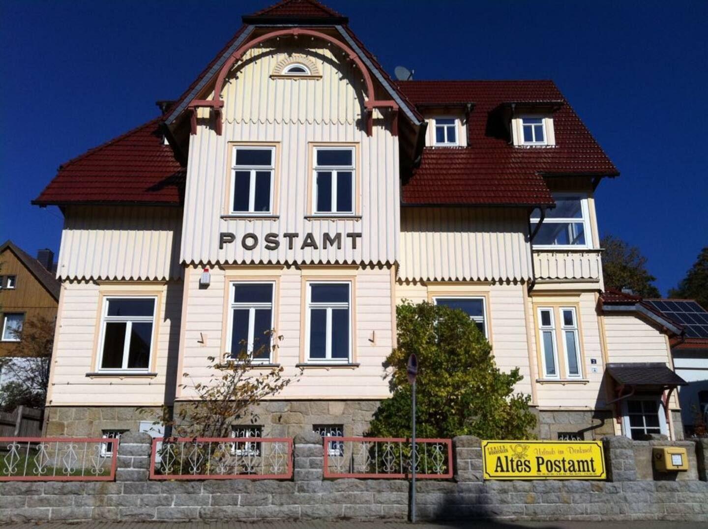 Altes Postamt mit rotem Dach und hellen Fassadenplanken.
