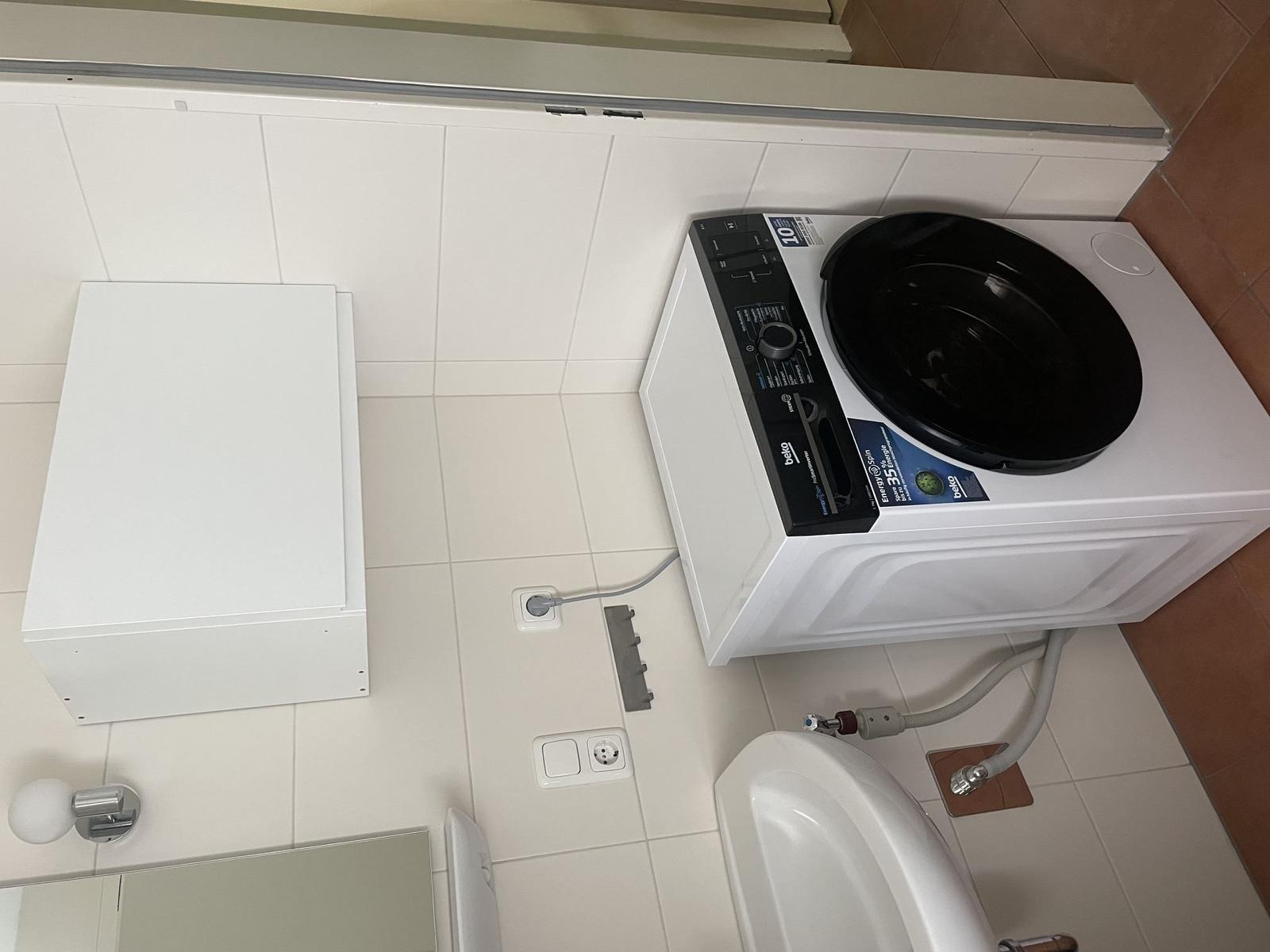 Waschmaschine mit Trockner in Badezimmer mit weißen Fliesen und Toilette