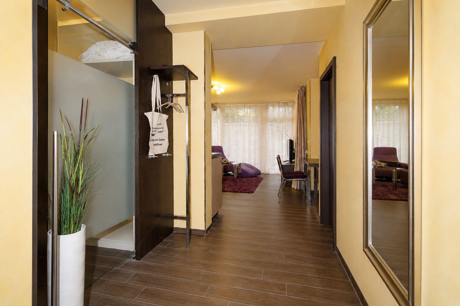 Flur mit Kleiderschrank, Pflanze und Blick in Wohnbereich mit Sitzgelegenheit.