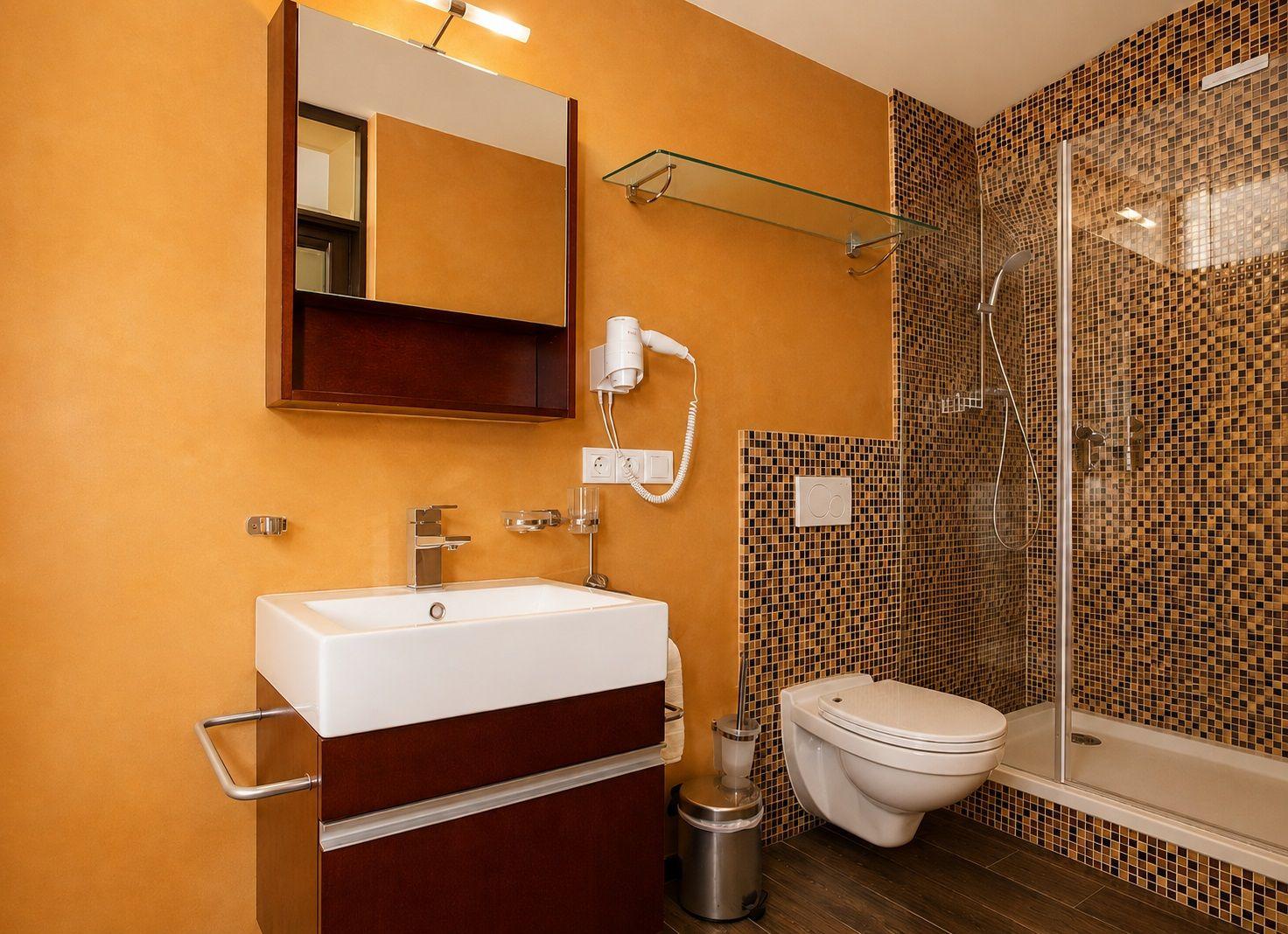 Bad mit Dusche, Waschbecken und Toilette. Wandverkleidung mit Mosaikfliesen.