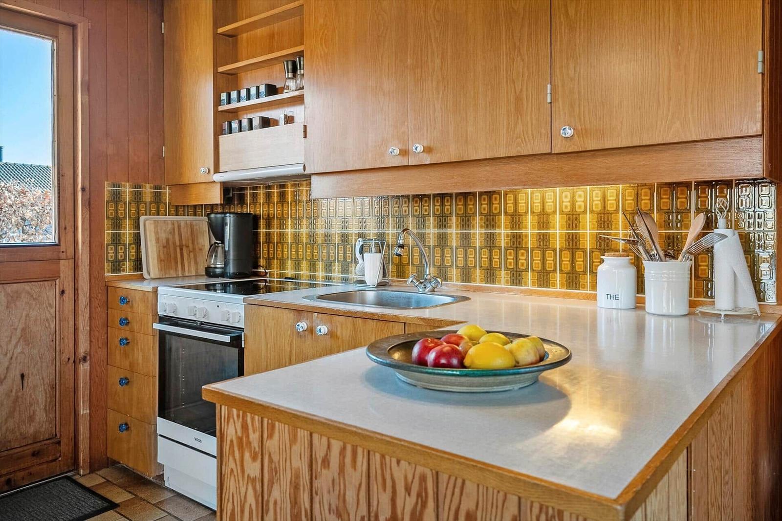 Küche mit Holzschränken, Mosaikwand und Obstschale auf Arbeitsplatte.