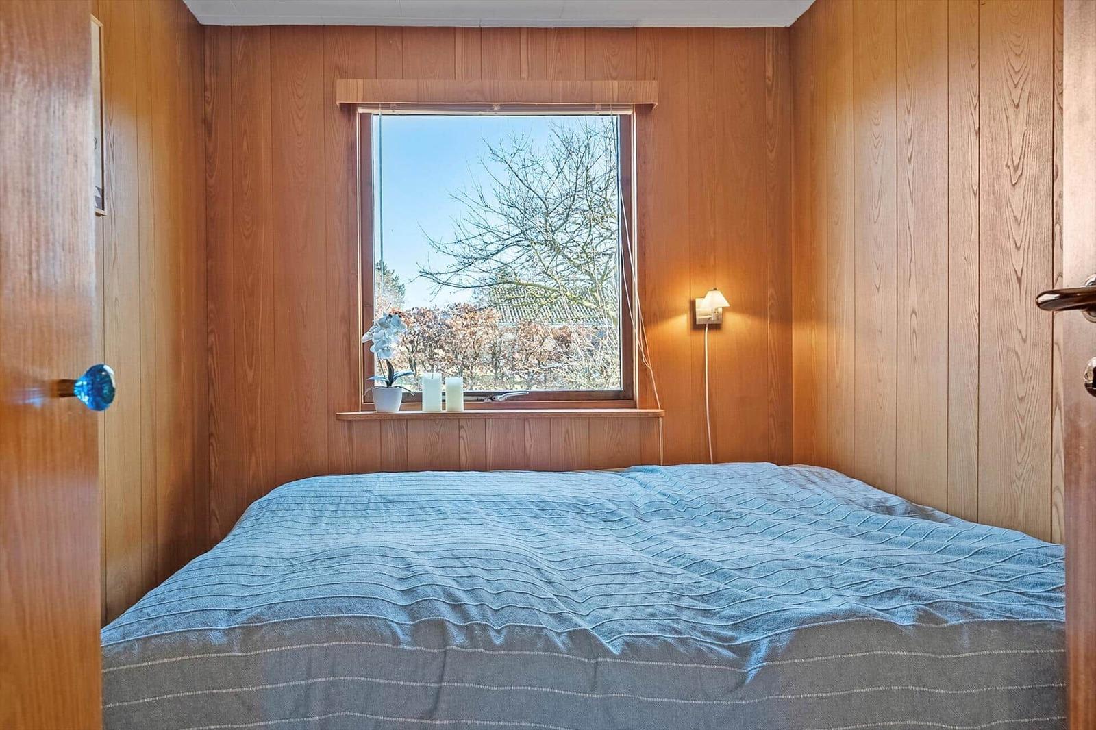 Schlafzimmer mit Holzwänden, Bett und Fenster mit Blick auf Bäume.
