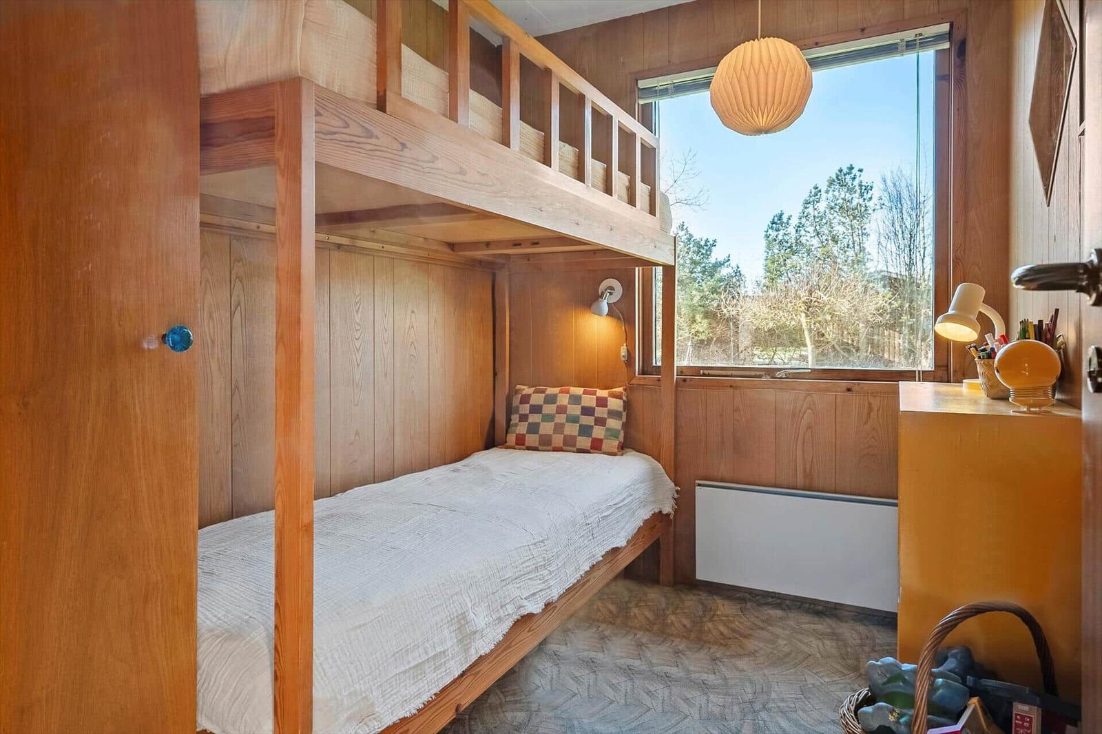 Ein Schlafzimmer mit Holzbett, Fenster und Schreibtisch.