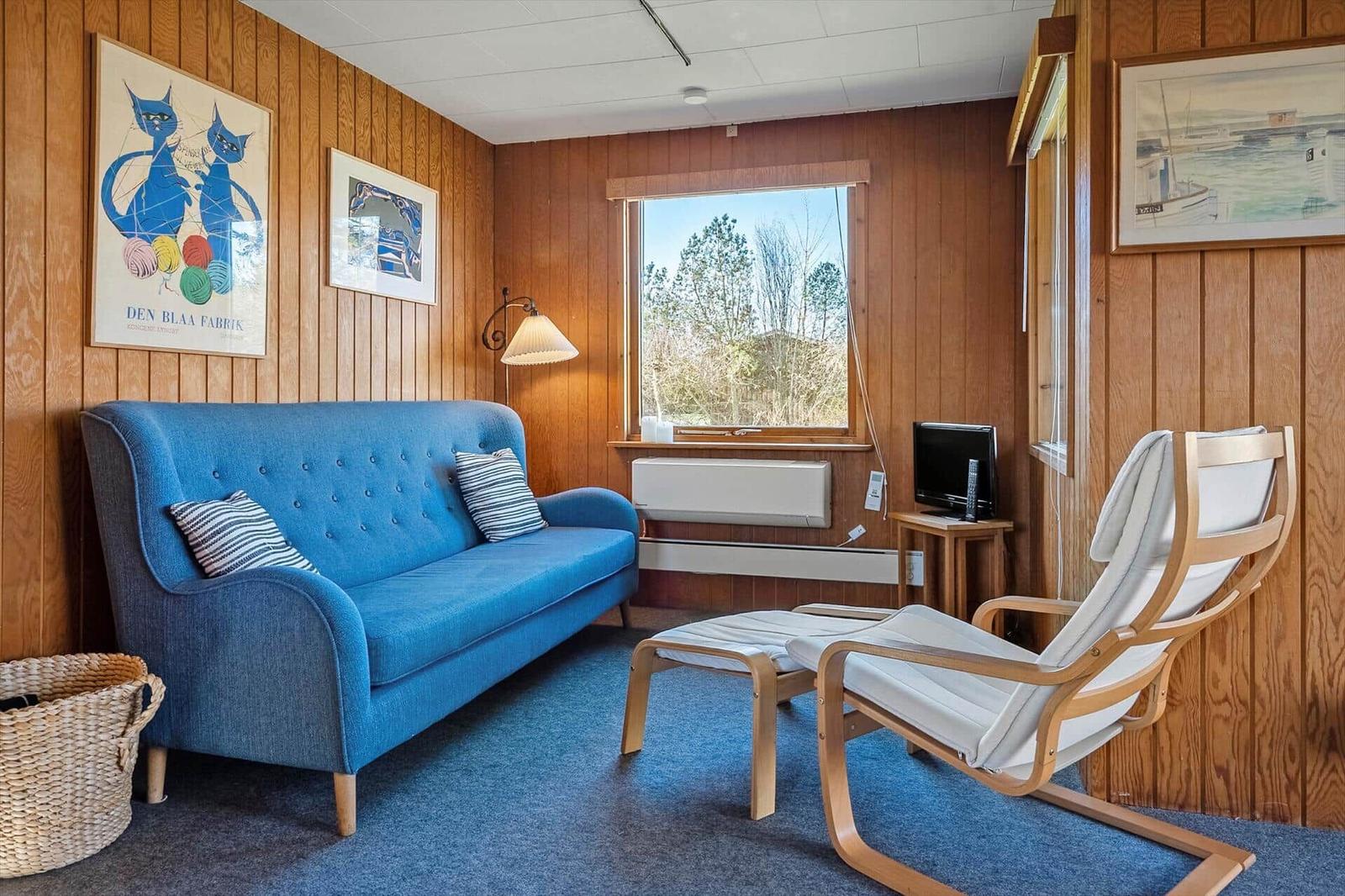 Ein Wohnzimmer mit blauem Sofa, Holzvertäfelung und Fensterblick auf Bäume.