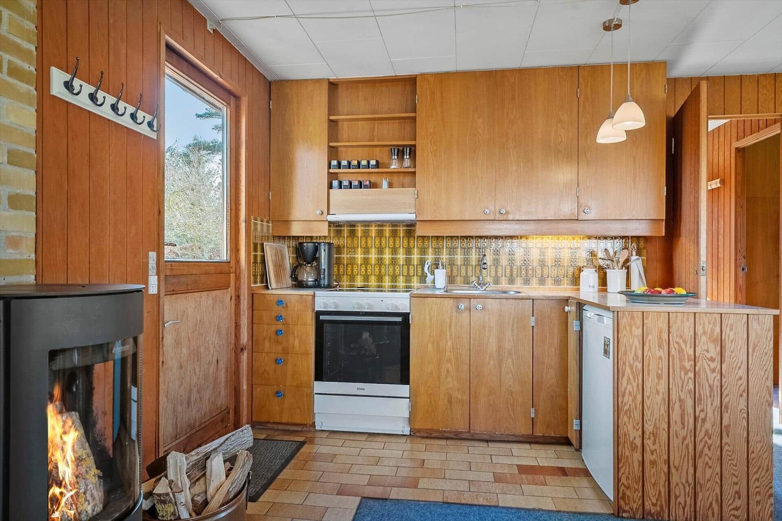Küche mit Holzschränken, Herd und Kamin im Vordergrund.