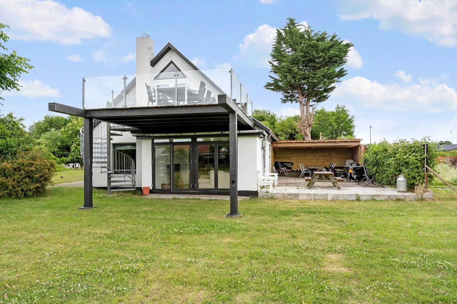 Moderne Villa mit Terrasse, Grillplatz und Garten. Glasdach und Holzveranda sichtbar.