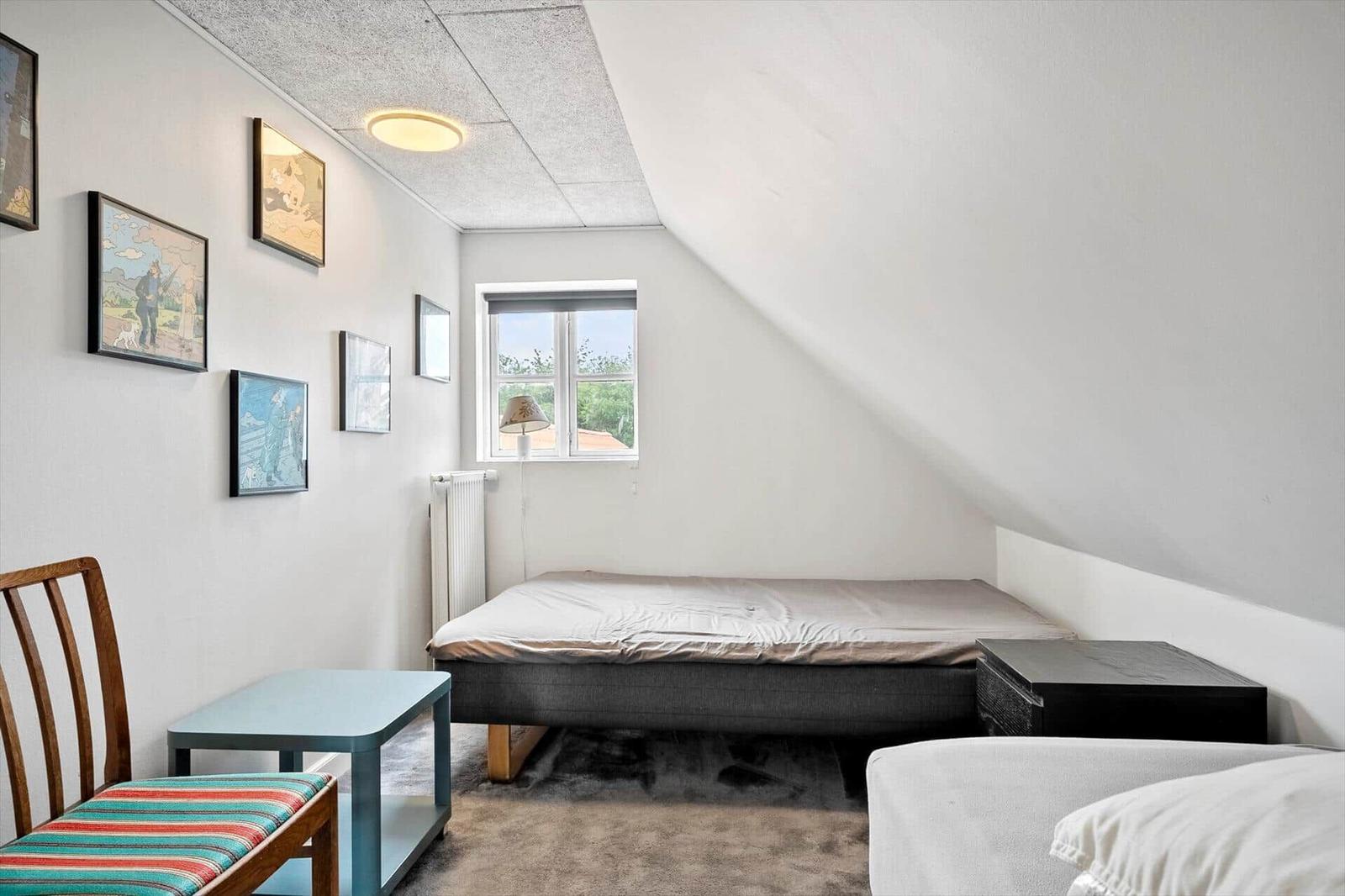 Zimmer mit Bett, Stuhl und Wandbildern unter schrägem Dach