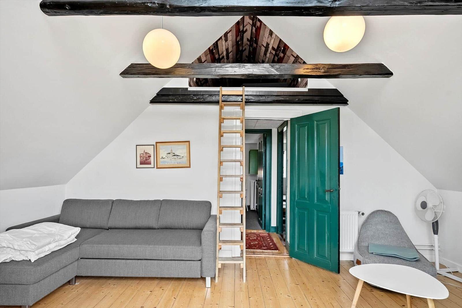 Wohnzimmer mit grafer Sofa, Holzboden und Leiter zur Dachbodenebene.