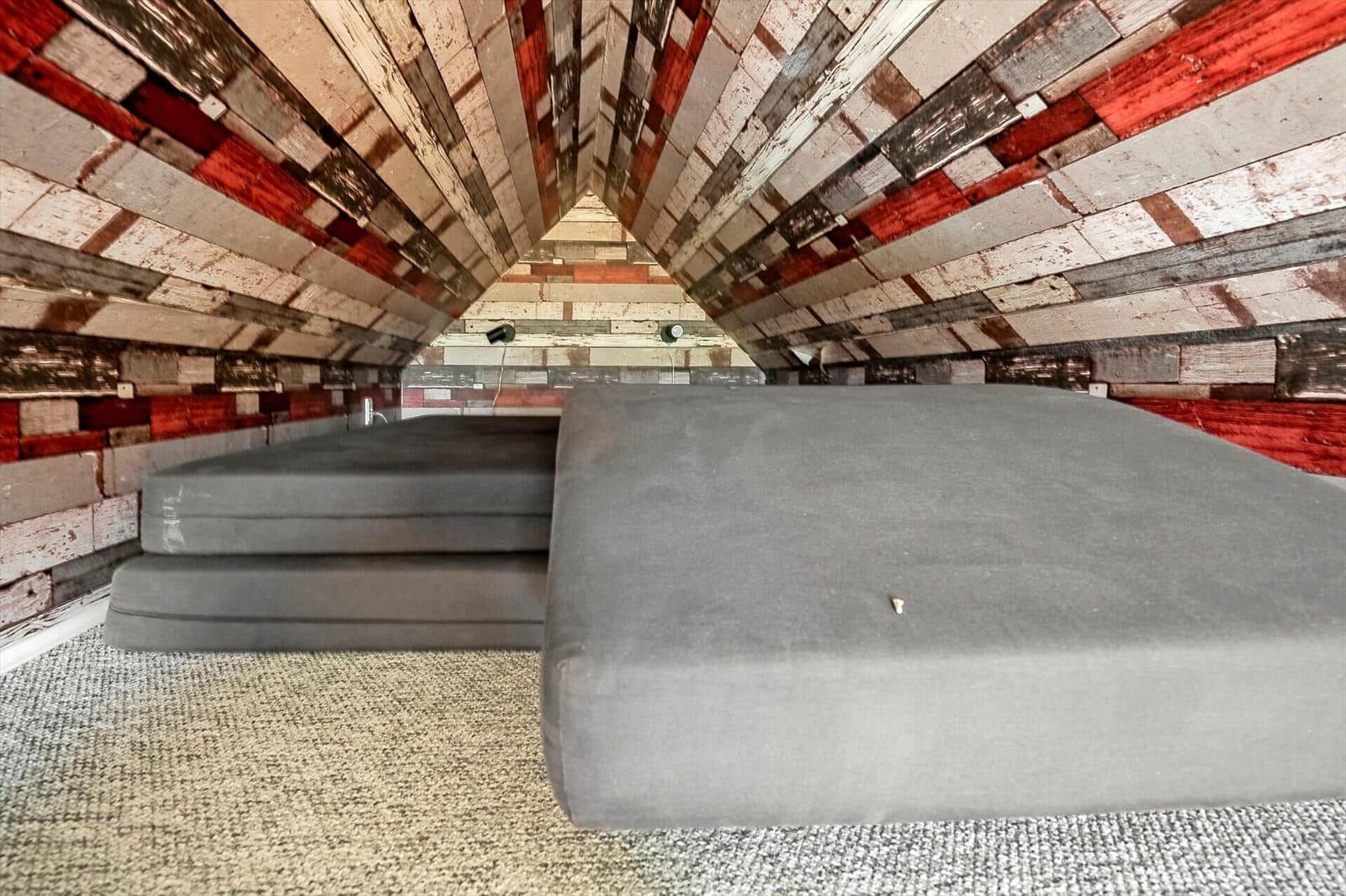 Zimmer mit Matratzen unter schrägen Holzwänden in verschiedenen Farben.