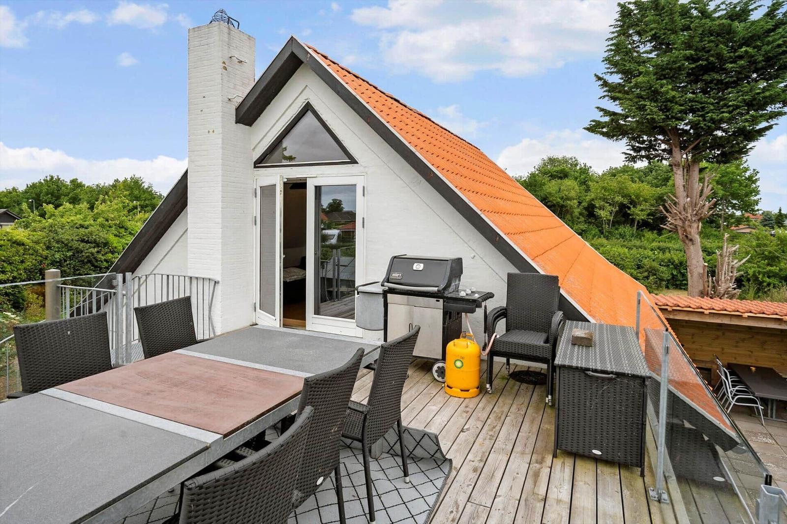 Terrasse mit Grill, Tisch und Stühlen vor einem Haus mit orangefarbenem Dach.