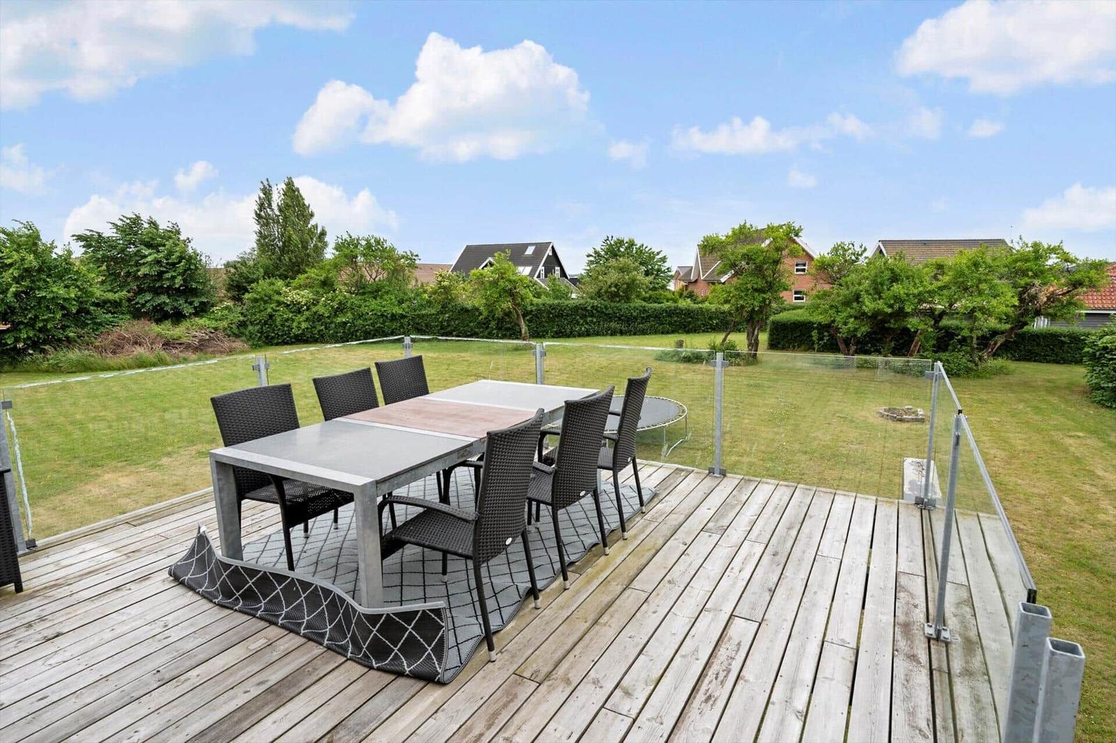 Terrasse mit Tisch und Stühlen, Blick auf grünen Garten und Häuser im Hintergrund.