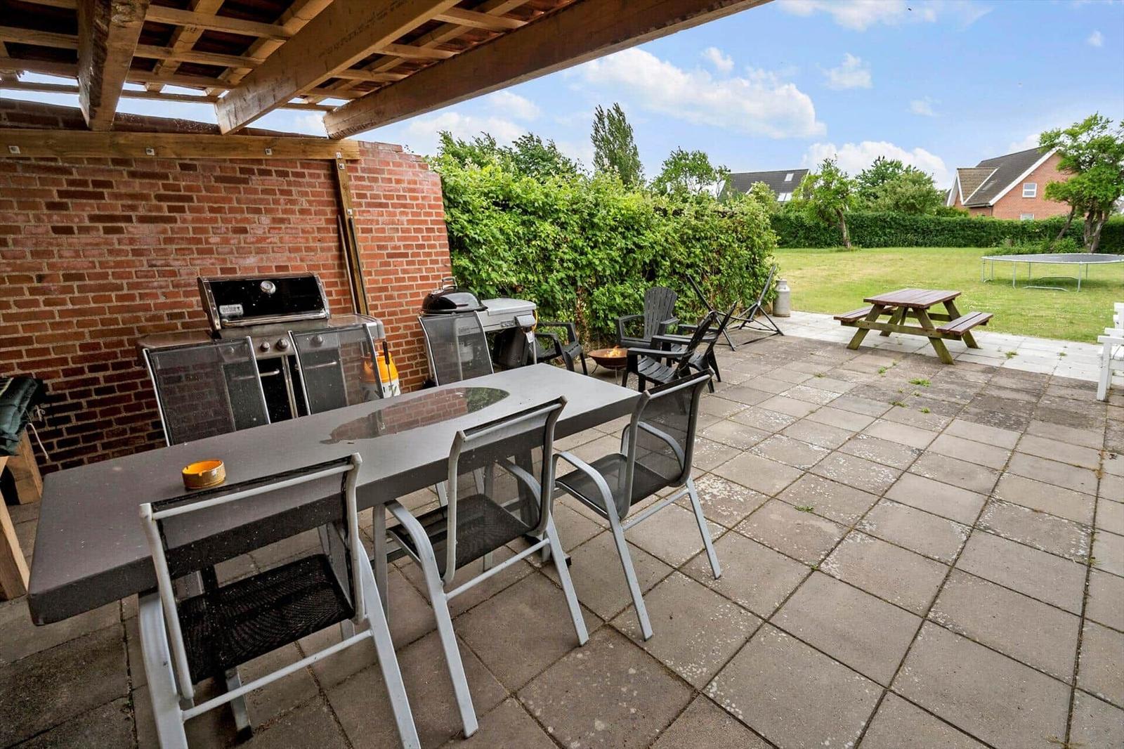 Terrasse mit Grill, Tisch und Stühlen. Im Hintergrund Grünfläche und Picknicktisch.