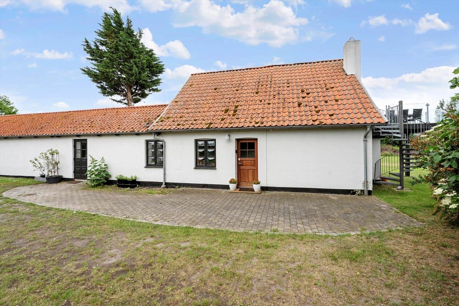 Wohnhaus mit rotem Ziegeldach, weißer Fassade und Holztür. Außenbereich mit Terrasse und Garten.