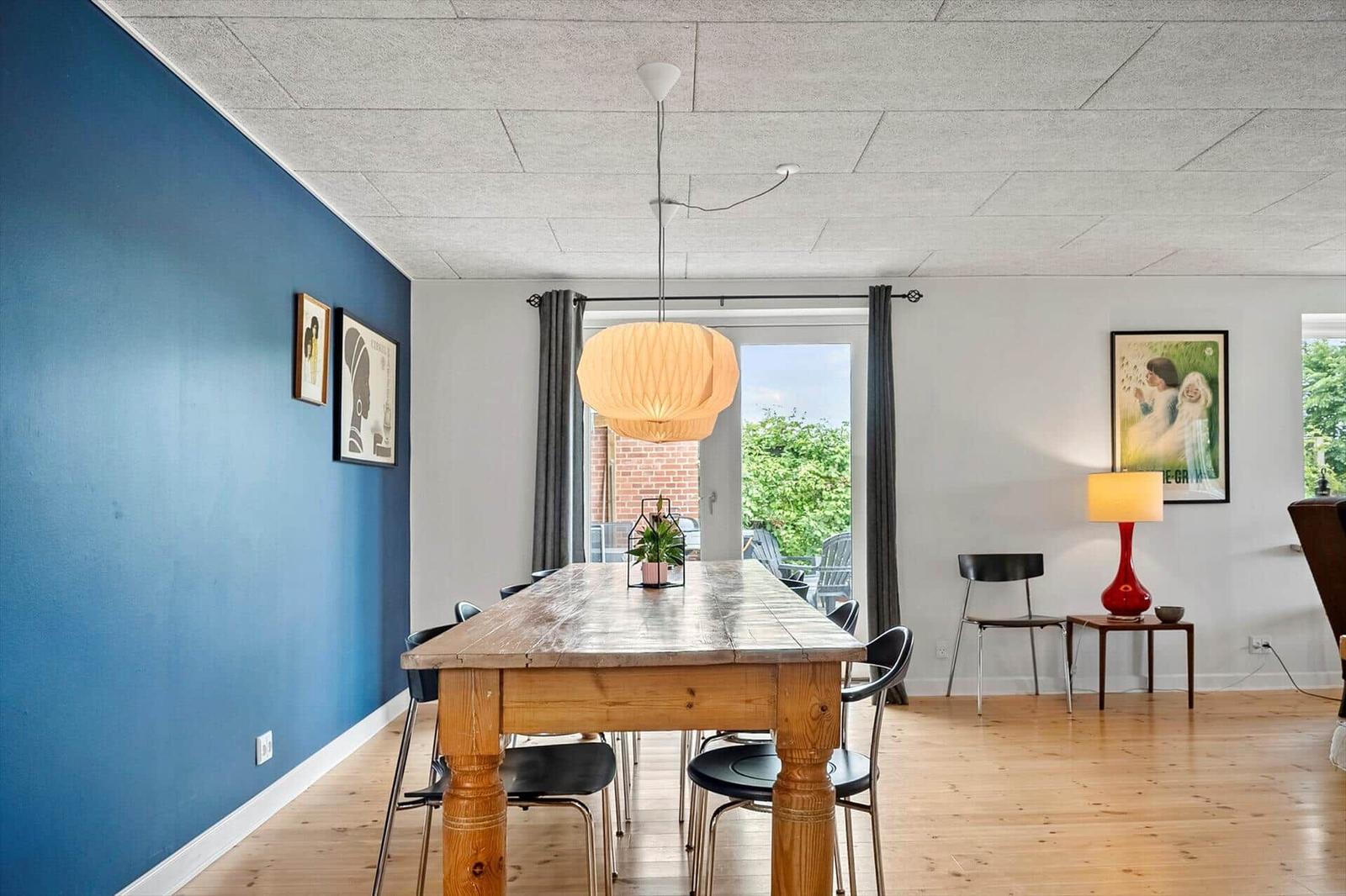 Esszimmer mit Holztisch, blauer Wand und Fenster zur Terrasse.