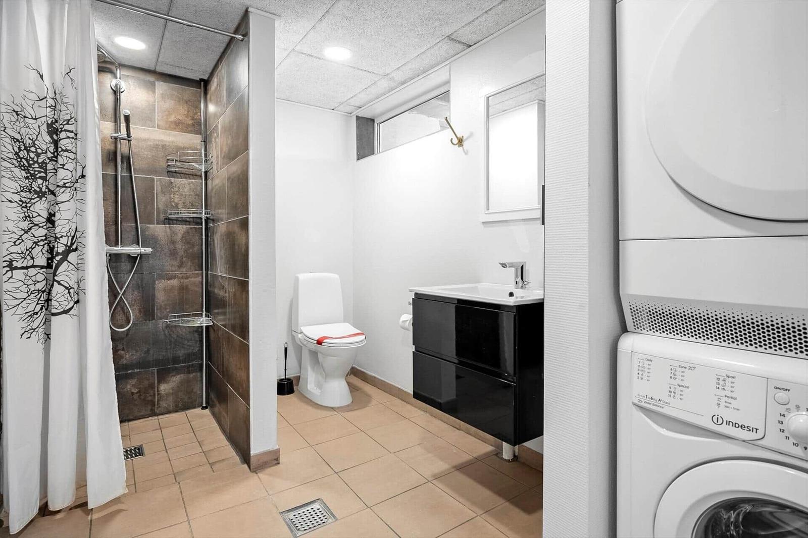 Badezimmer mit Dusche, Toilette und Waschbecken. Nebenbei steht eine Waschmaschine.
