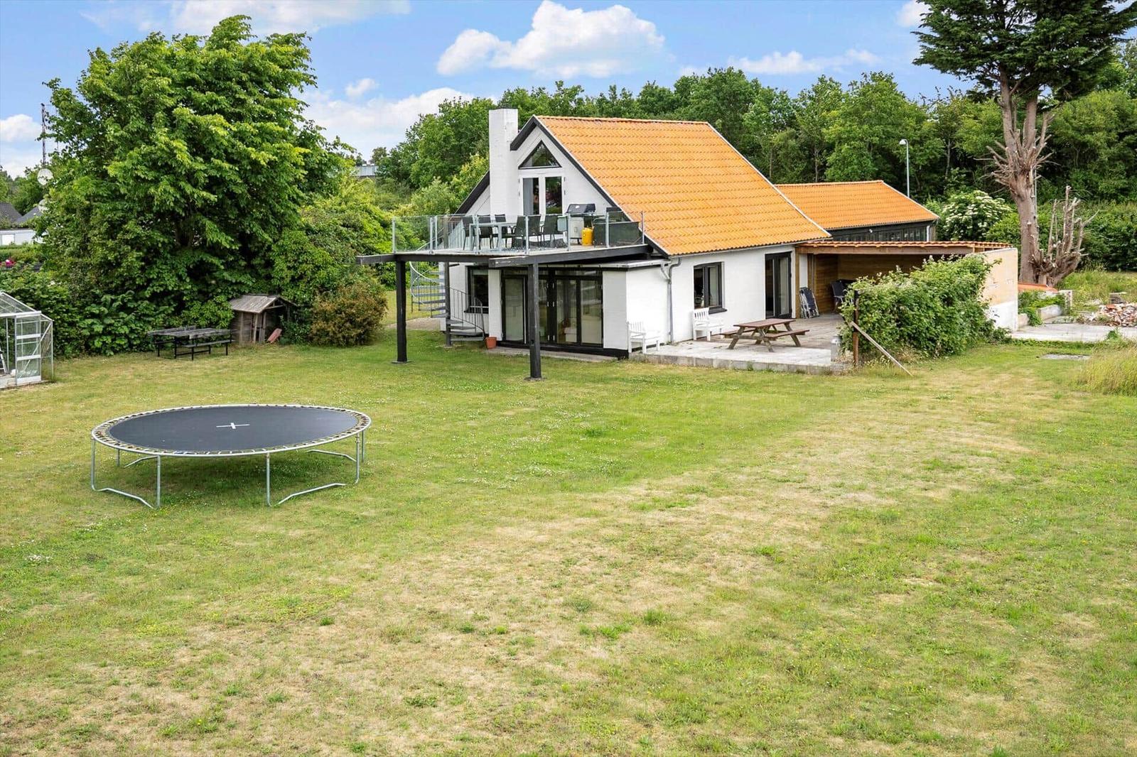 Haus mit Terrasse, Grill und Trampolin auf grünem Grundstück.