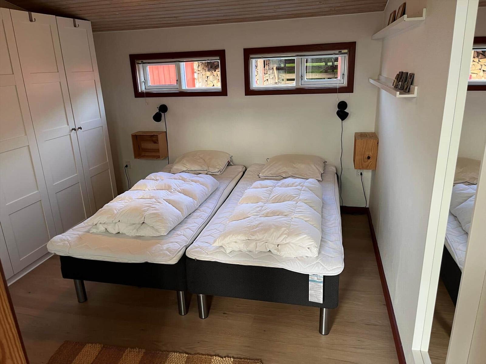 Two beds with white bedding, two windows, closet and wall shelves.