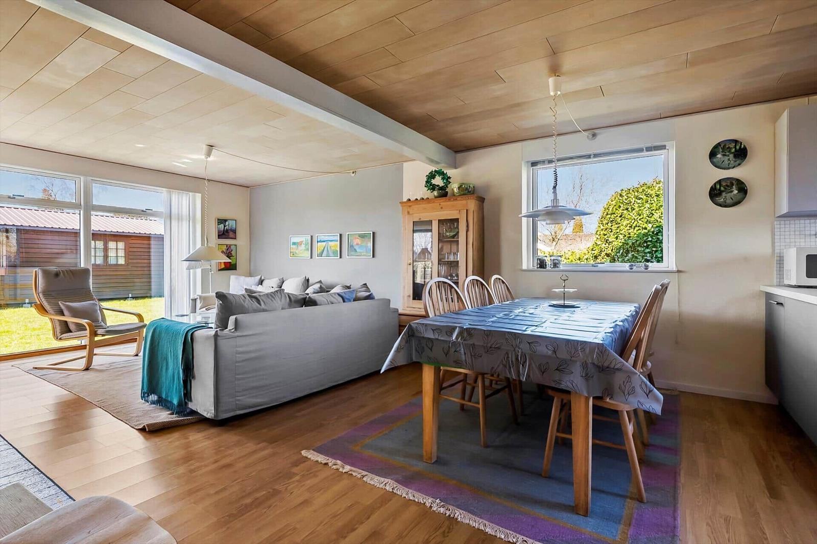 Wohn- und Essbereich mit Holzdecke, Sofa, Esstisch und Fenster zur Außenterrasse.