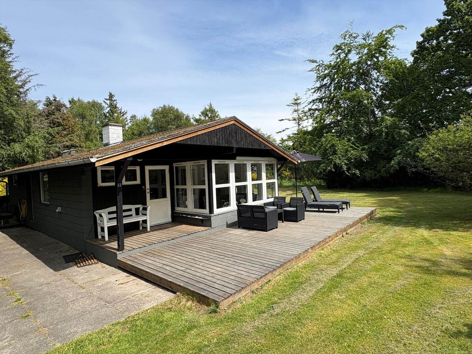 Holzhaus mit Terrasse, Garten und Liegestühlen. Modernes Design mit großem Fensterbereich.
