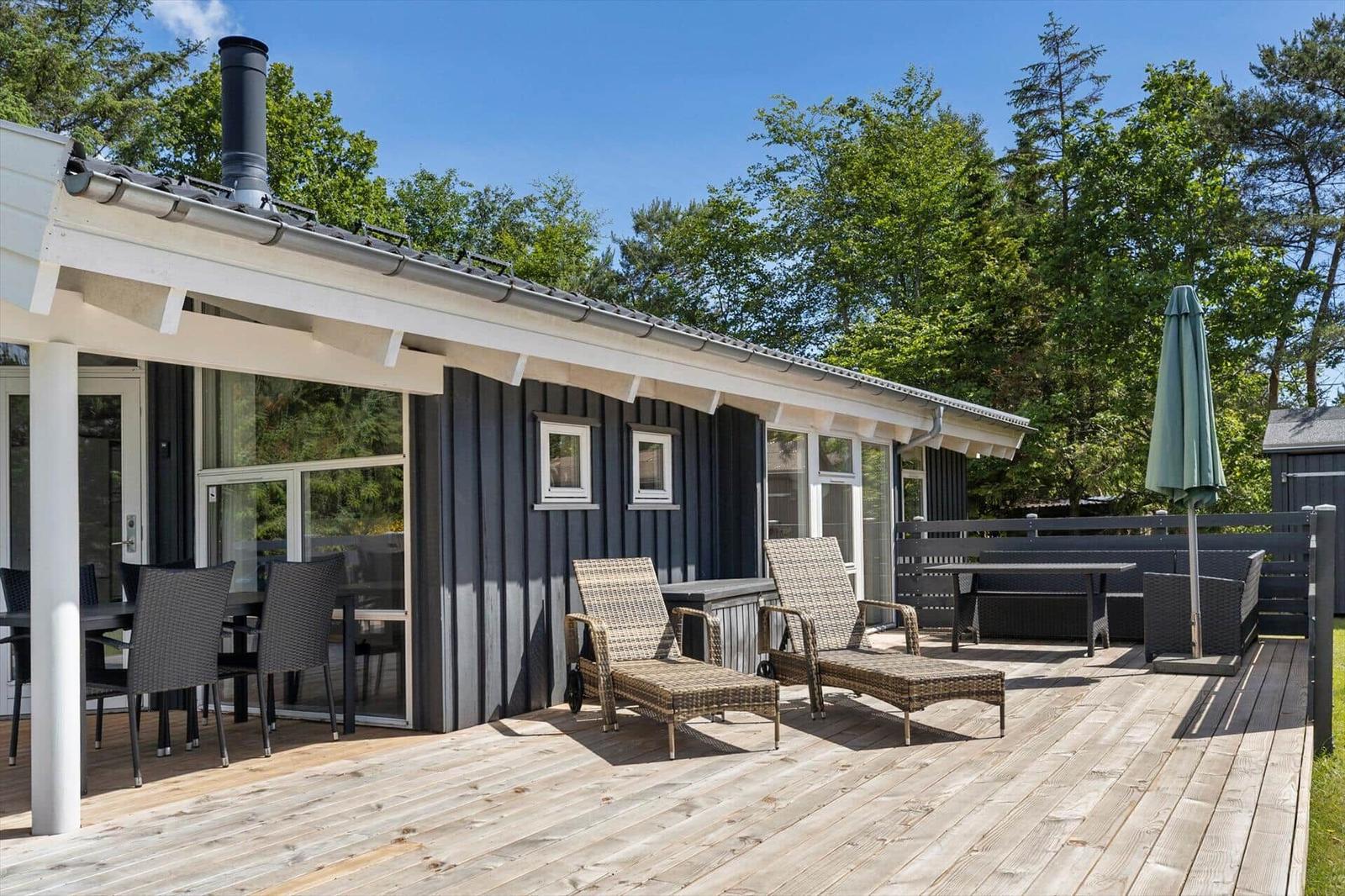 Deck with lounge chairs, table, and umbrella in front of a house with wooden veranda.