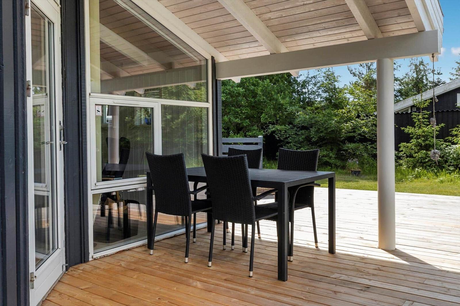Patio with table and chairs under roof, view of green garden.