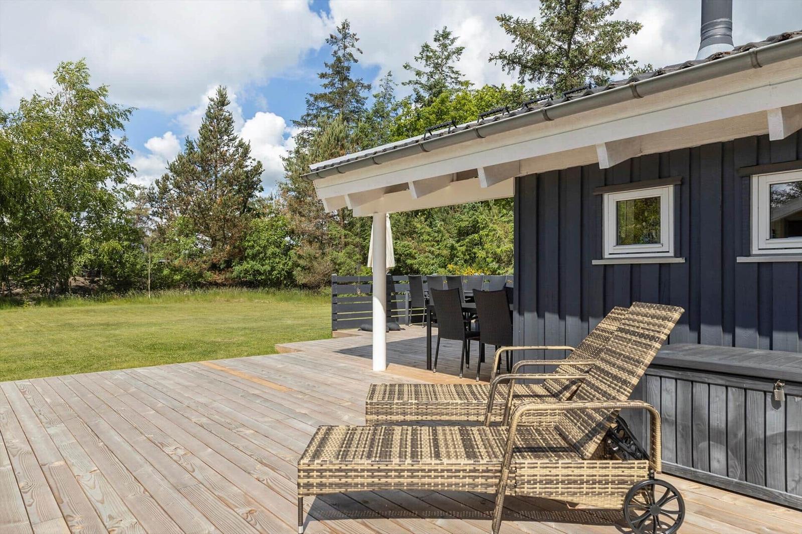 Deck with lounge chairs, table and chairs next to a house with dark siding.
