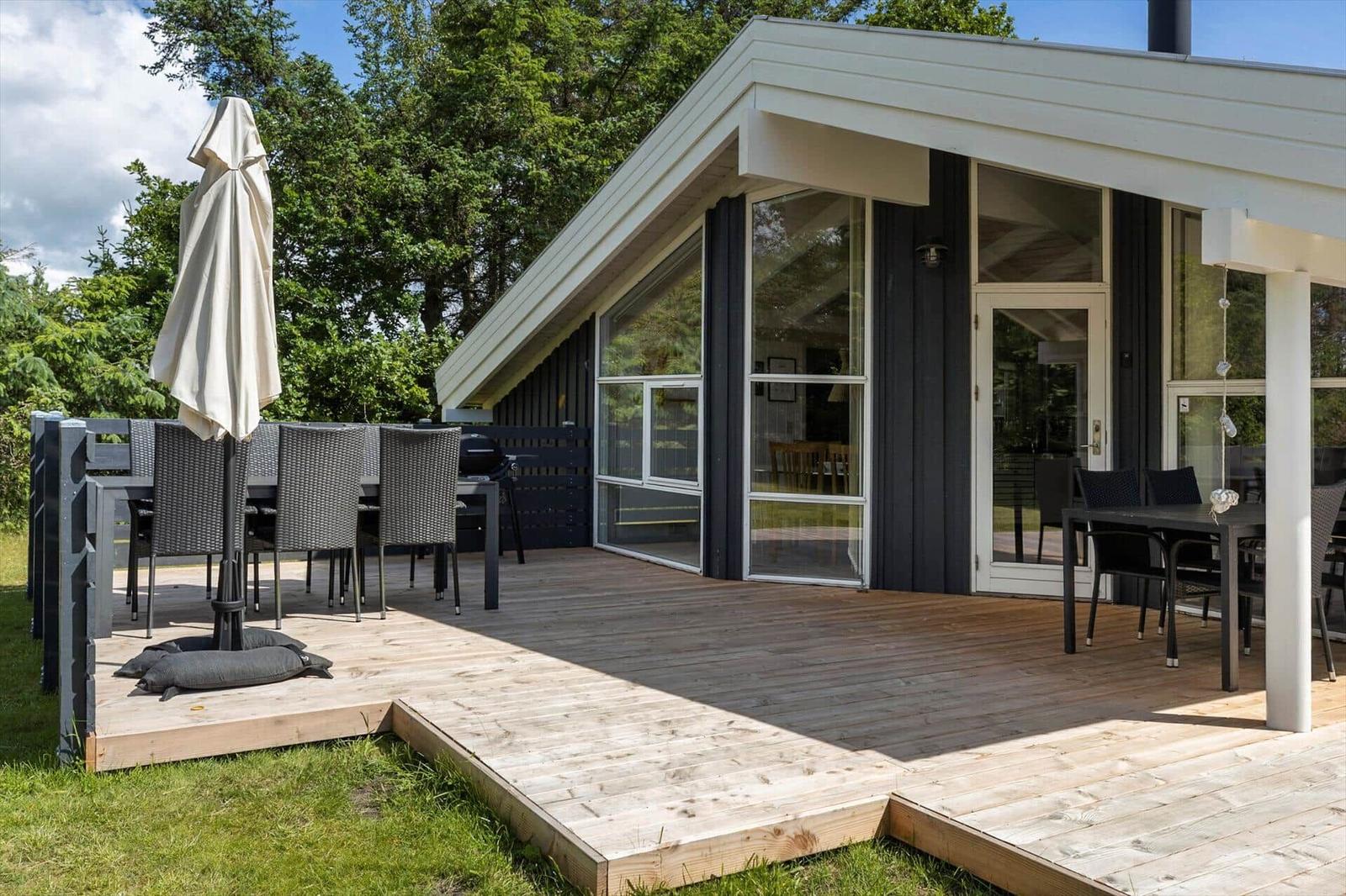 Modern villa with terrace, grill, and outdoor table. Surrounded by trees and grass.