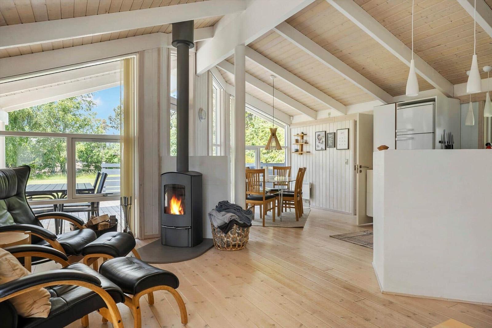 Living area with fireplace, dining area, and kitchen. Wooden floor and large windows.