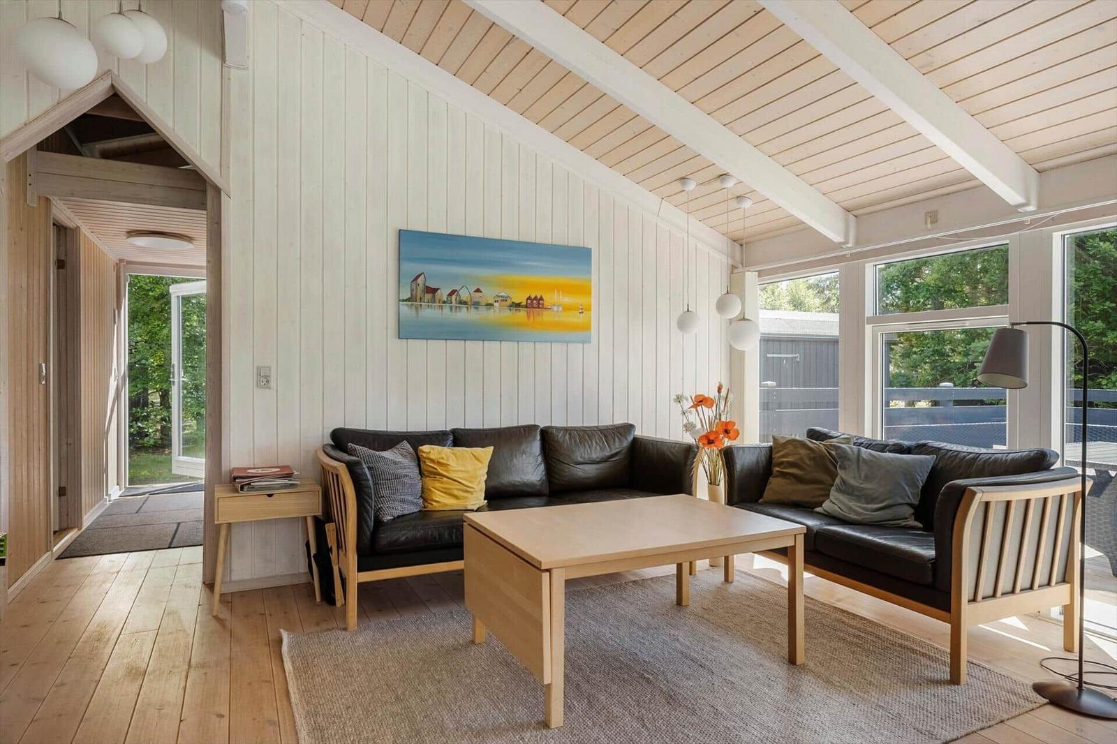 Living room with two leather sofas, wooden table, and wall art. Wooden ceiling and large windows.
