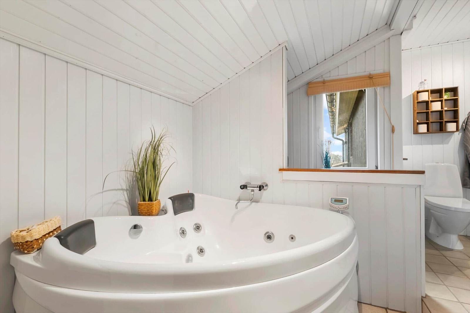Dusche mit Whirlpoolbad, Pflanze und Fenster mit Blick nach draußen.