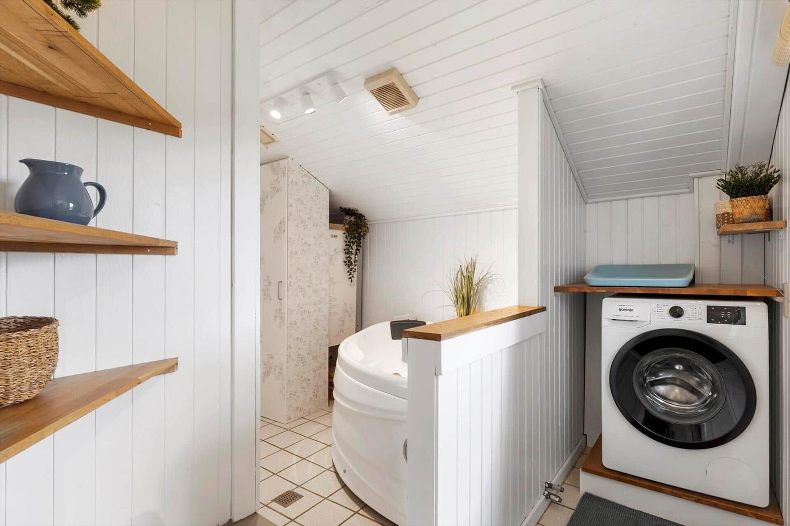 Badezimmer mit Badewanne, Waschmaschine und Holzregalen an weißen Wänden.