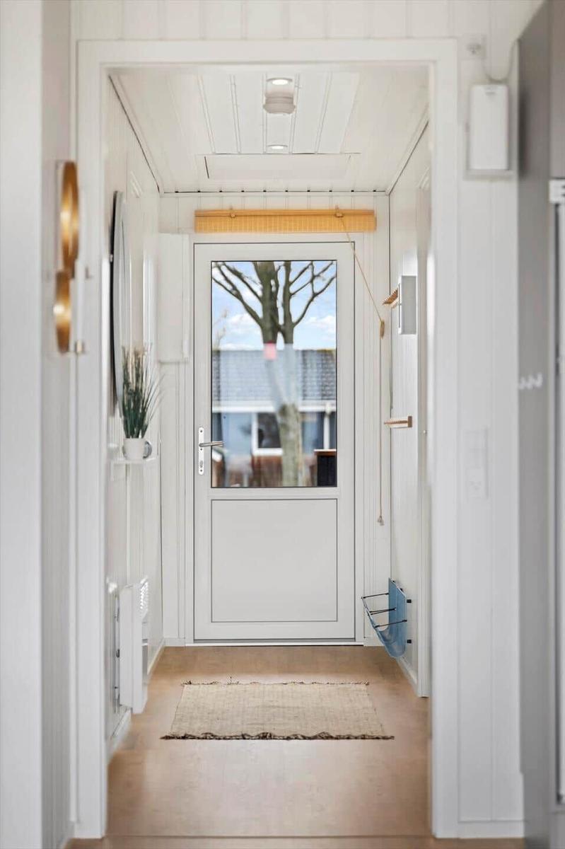Hausgang mit weißen Wänden, Holzboden und Tür mit Glasfenster. Vor dem Fenster steht ein Baum.
