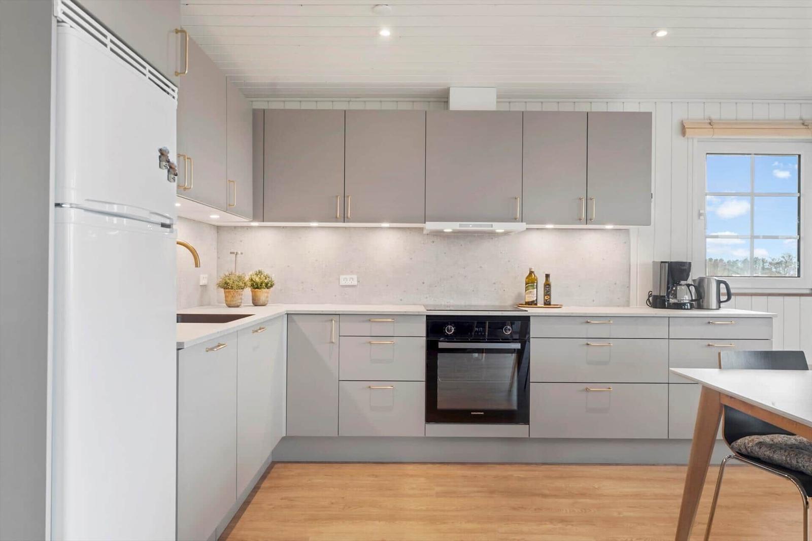Moderne Küche mit grauen Schränken, weißem Kühlschrank und Holzboden.