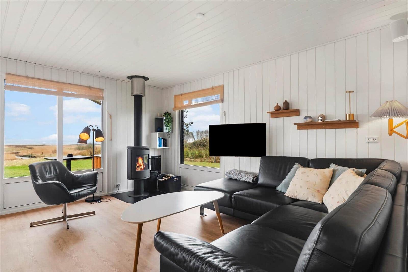 Wohnzimmer mit Sofa, Kamin und TV. Große Fenster mit Blick auf Landschaft.