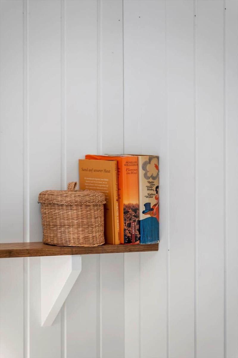 Holzregal mit Korb und Büchern an weißer Wand