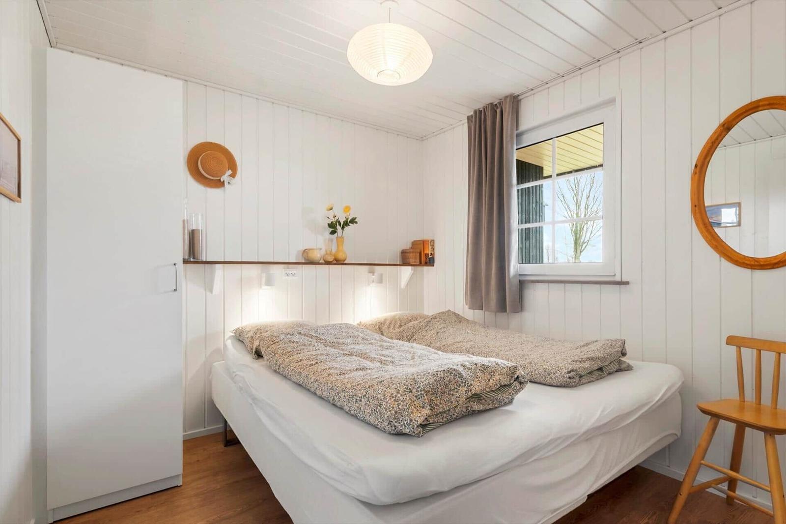 Schlafzimmer mit Bett, Kleiderschrank, Fenster und Holzstuhl.