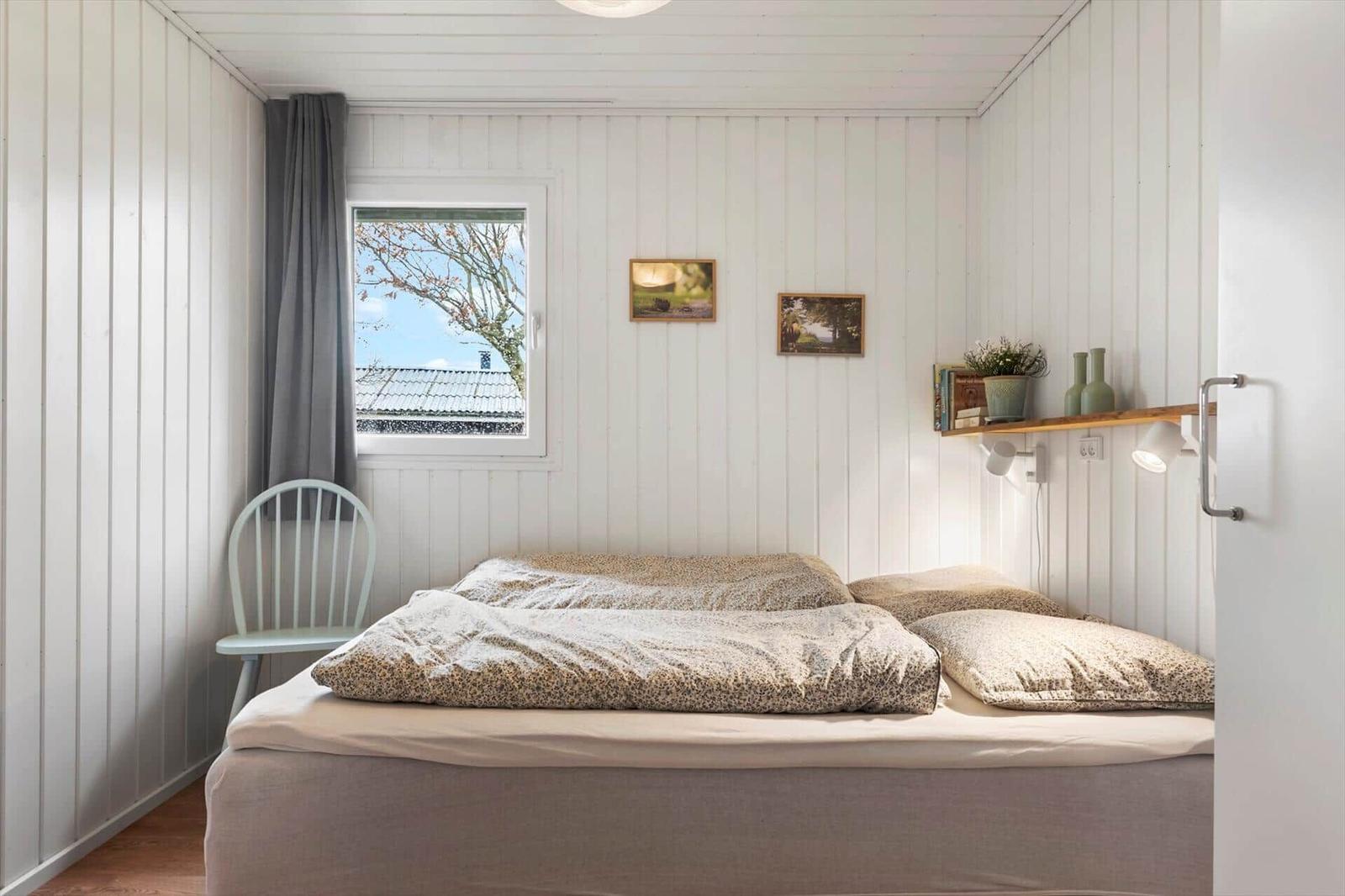 Schlafzimmer mit Bett, Fenster, Stuhl und Wandregal.