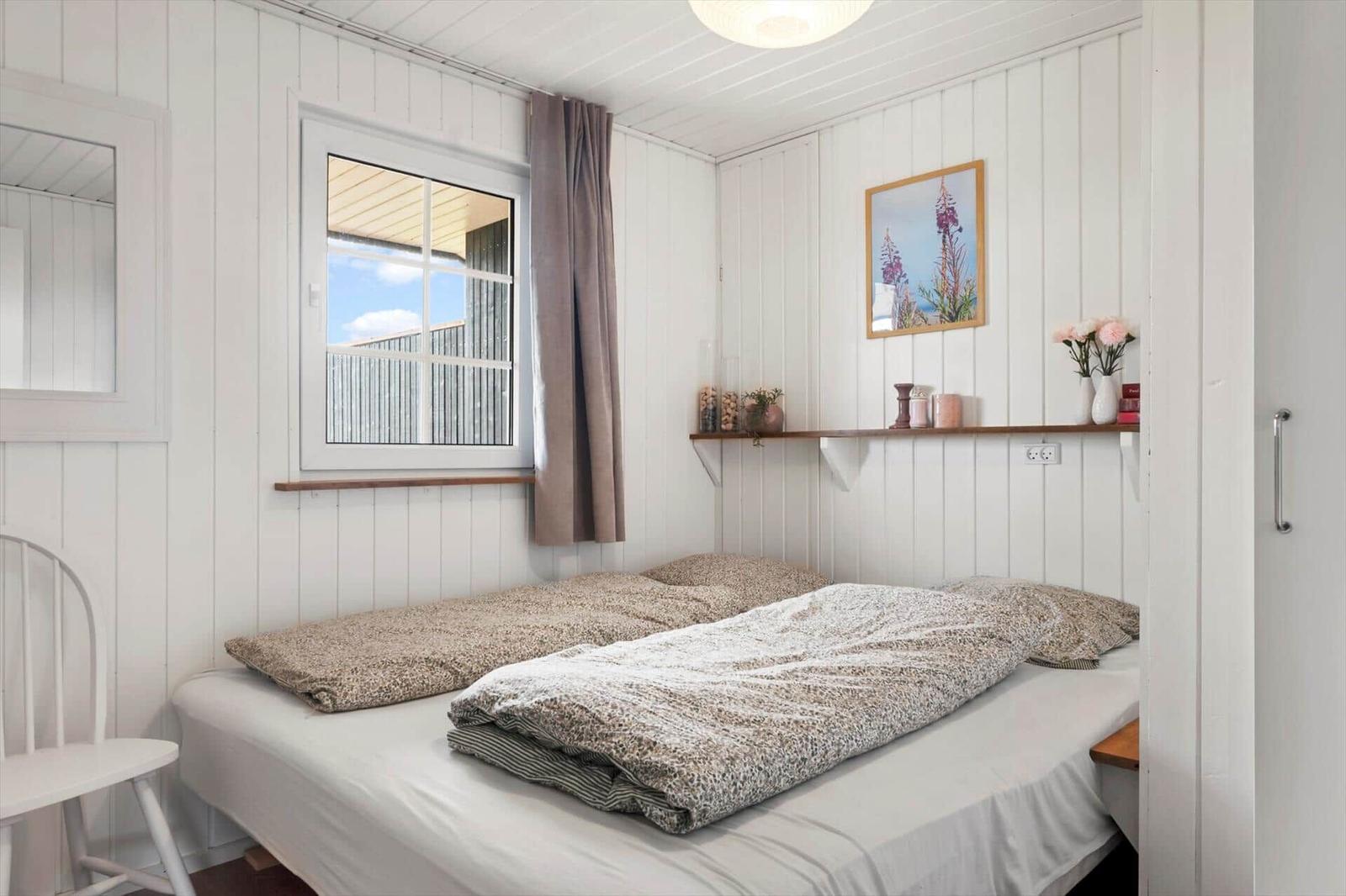 Schlafzimmer mit Bett, Fenster und Wandregal. Weiße Holzwände und Decke.