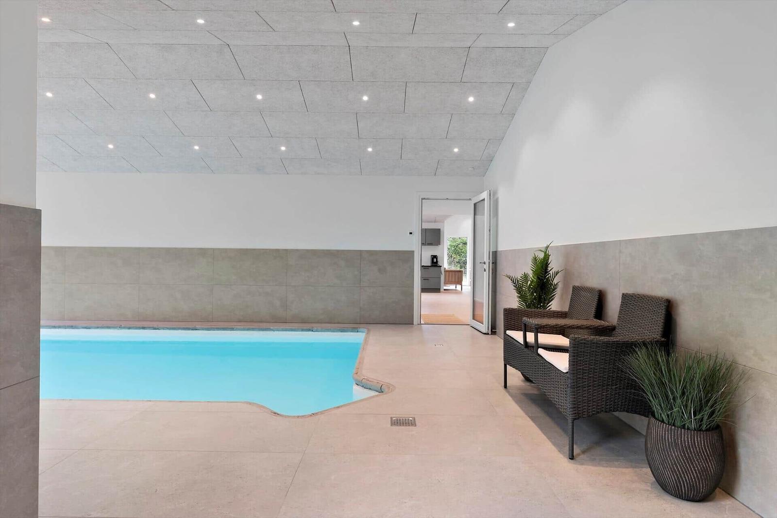 Innere Schwimmhalle mit Pool, Sitzgelegenheiten und Pflanzen.