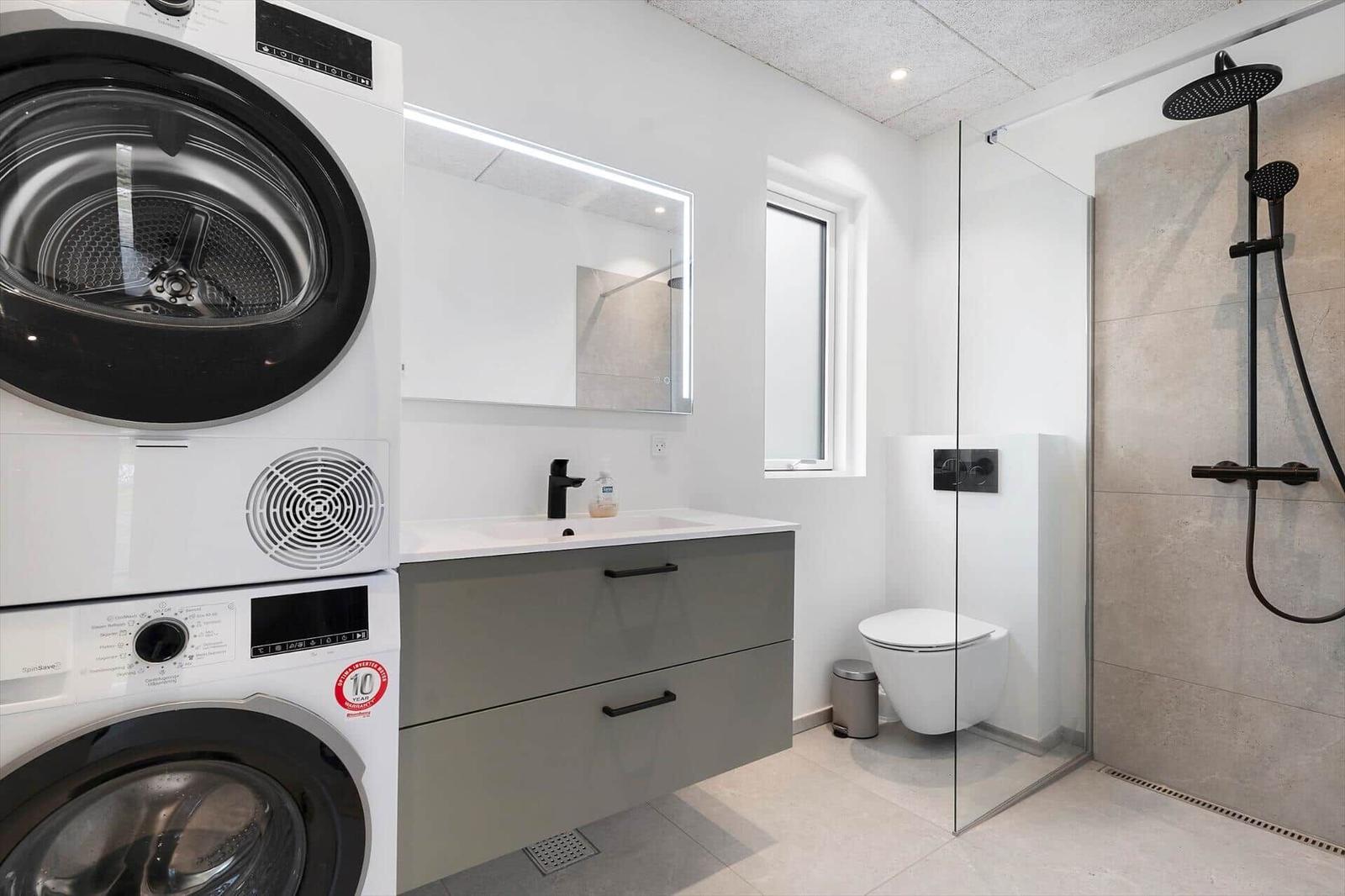 Badezimmer mit Dusche, Waschbecken und Waschmaschine.