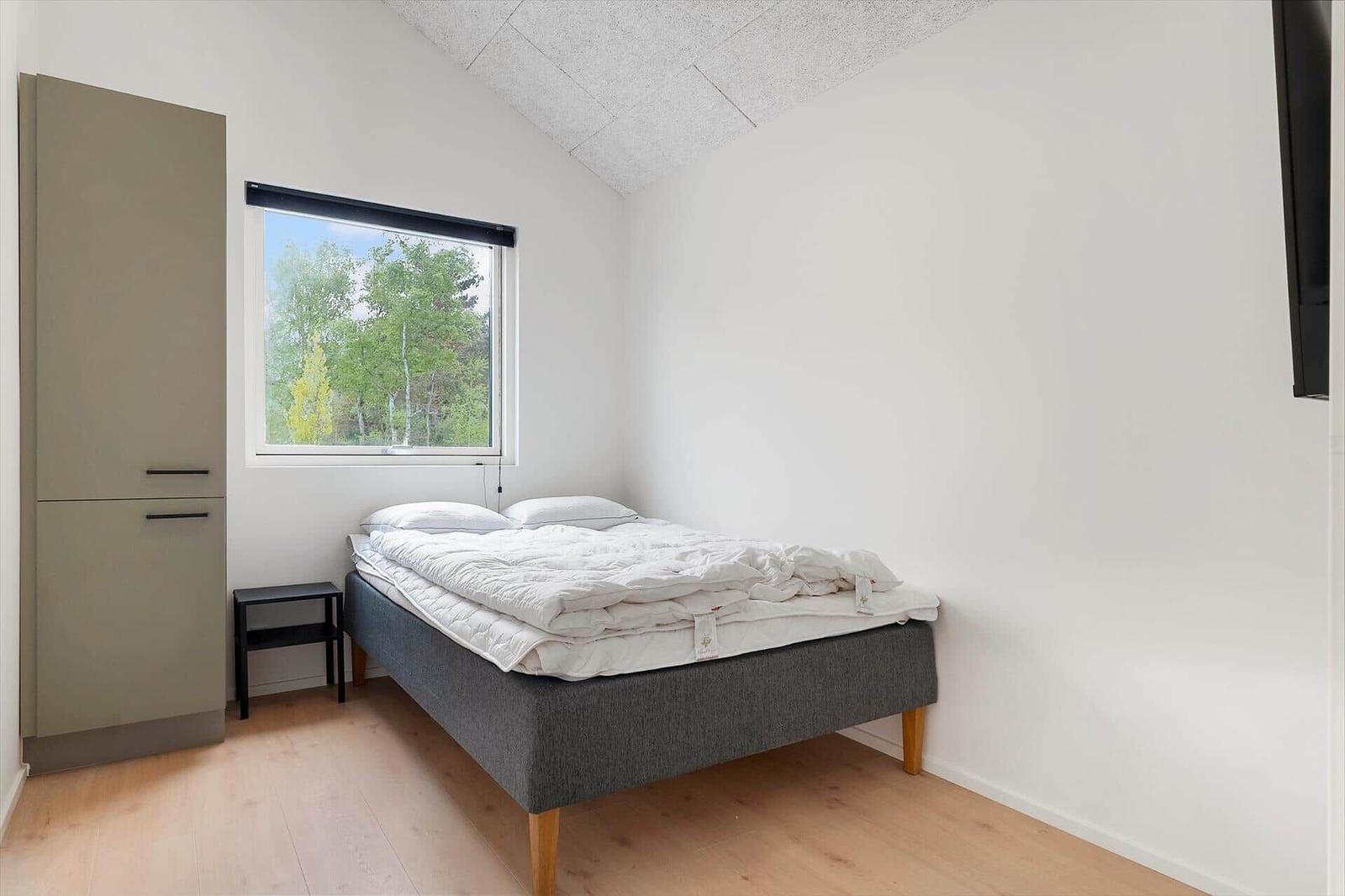 Schlafzimmer mit Bett, Kleiderschrank und Fenster zum Wald.