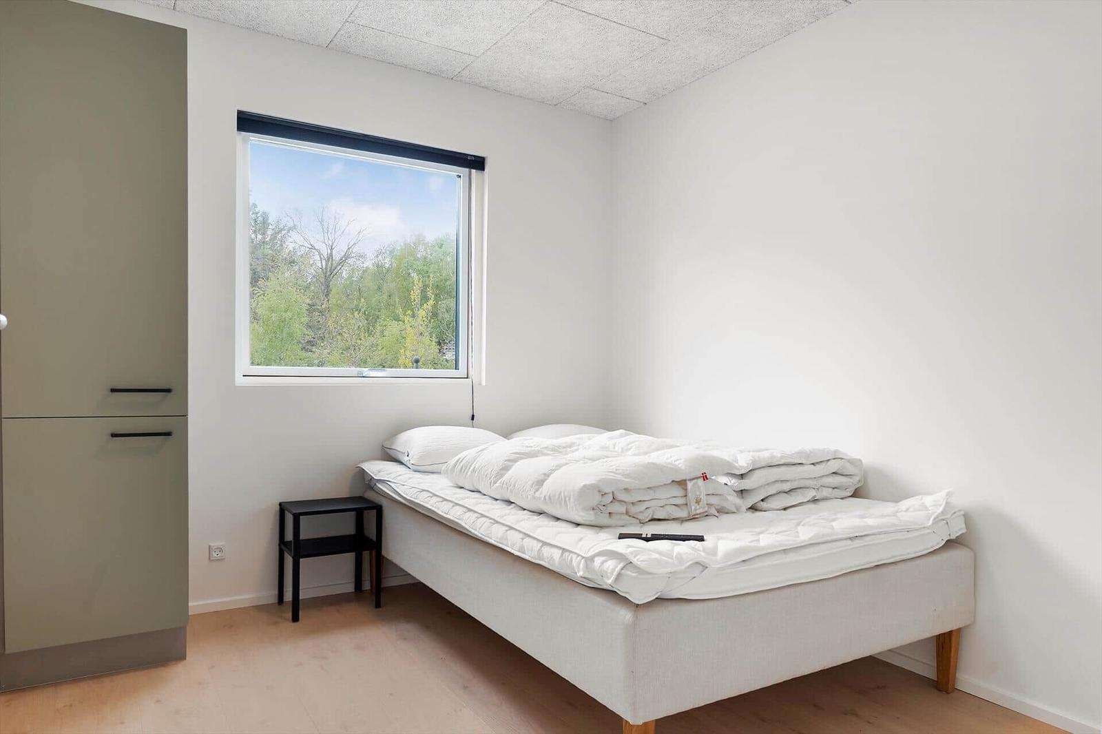 Schlafzimmer mit Bett, Kleiderschrank und Fenster mit Blick auf Bäume.