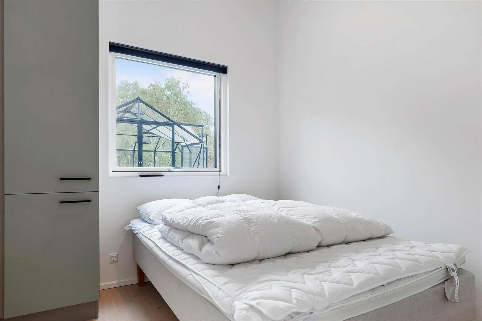 Schlafzimmer mit Bett, Fenster und Kleiderschrank. Draußen ist ein Glasbau sichtbar.