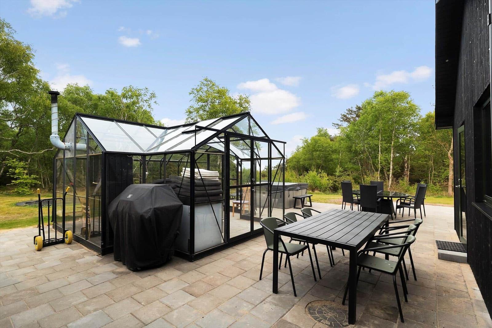 Außenbereich mit Glasgewächshaus, Grill und Sitzgruppe auf Steinplatten