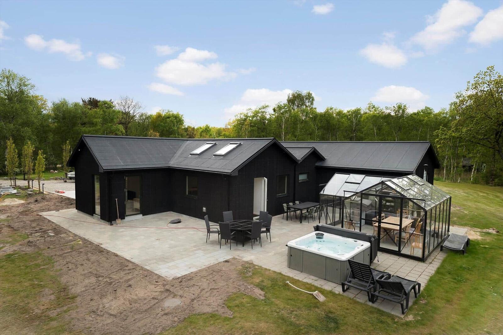 Schwarzes Haus mit Pool, Terrasse und Glasüberdachung. Umgeben von Grün und Bäumen.