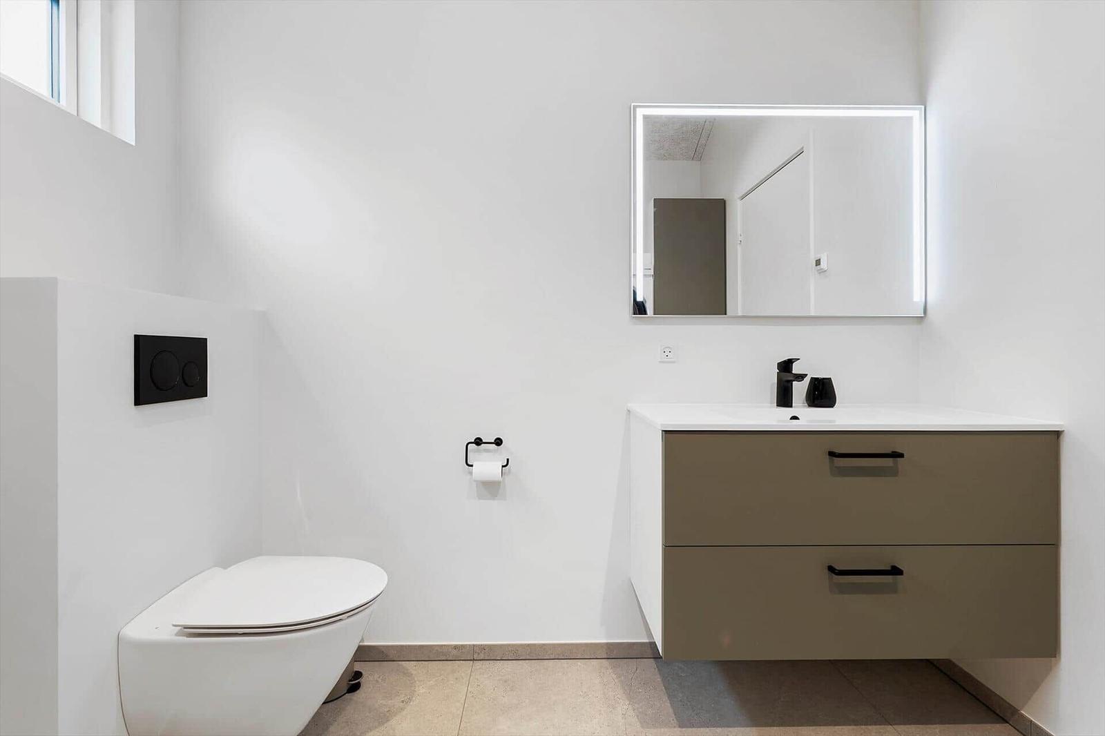 Moderne Badezimmer mit Toilette, Waschbecken und beleuchtetem Spiegel.