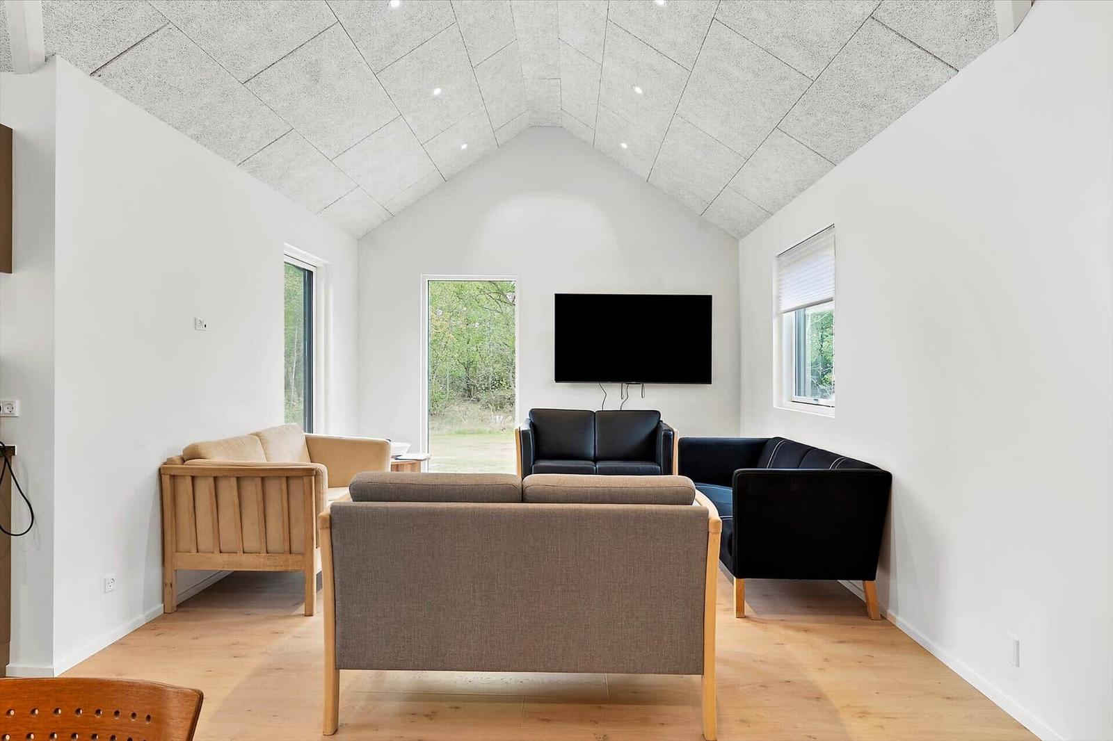 Wohnzimmer mit Sofa, Sesseln und Fernseher. Holzboden und hohes Dach.